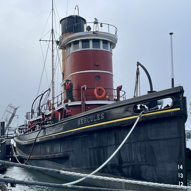 a large red steam tug boat is moored to a pier
