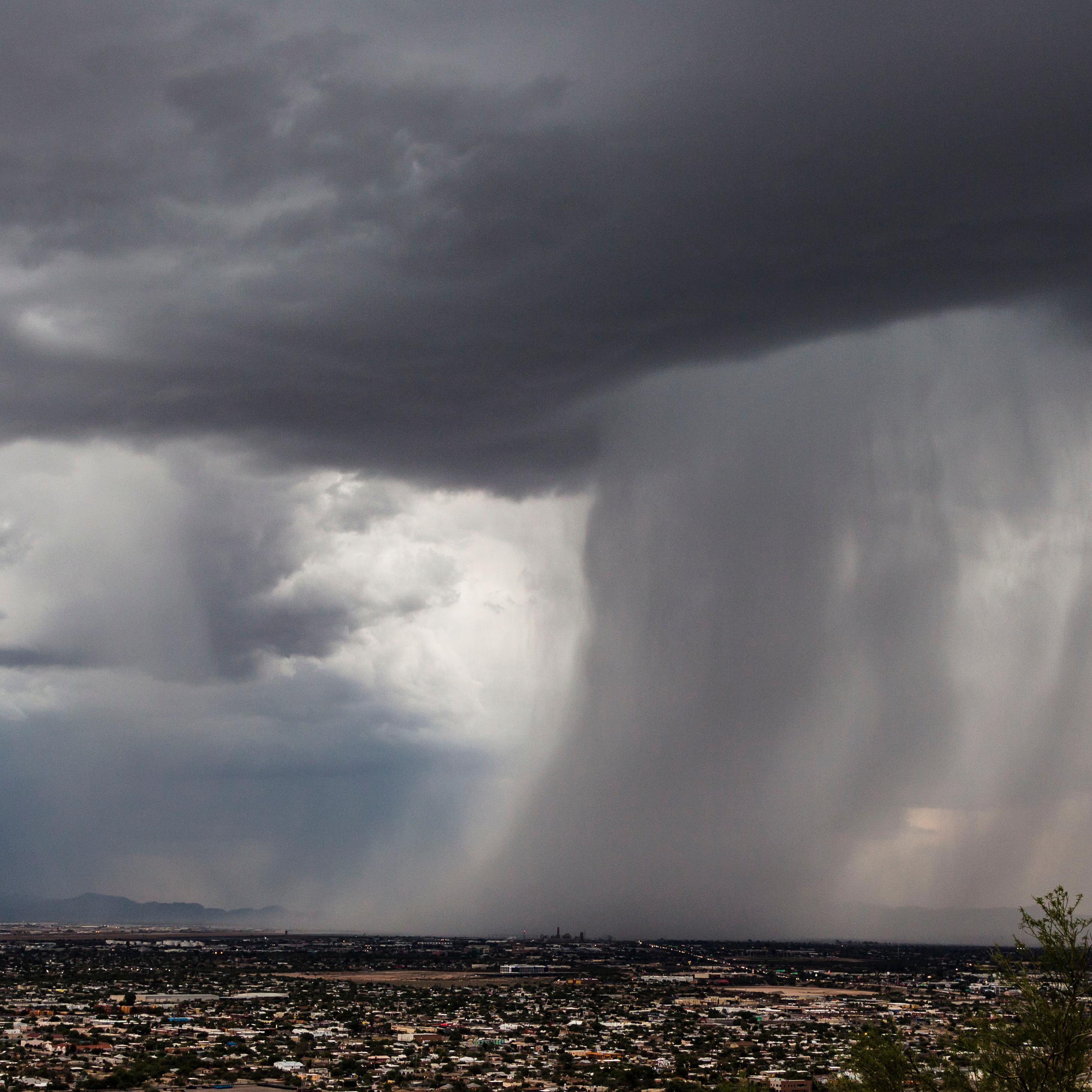 Image looks out over the city of Tucson. A large storm cloud rolls in from the right, dumping water.