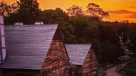 orange sunrise over two wood-sided buildings with paths leading between them