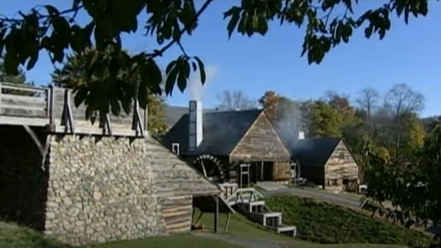 A wood and stone bridge with two wood buildings that each have chimneys releasing smoke