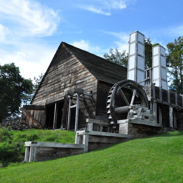 large single-story wooden building with white chimneys and water wheels on either side of entrance