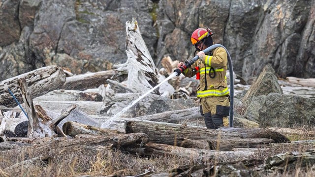 A firefighter sprays water on smoldering driftwood
