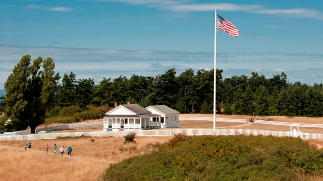 Historic white buildings in a fenced area with an American flag.