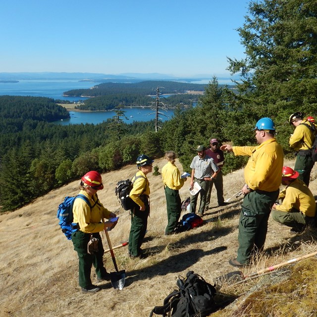 A fire crew and park staff discuss presrciption burn plans on a grassy hill.
