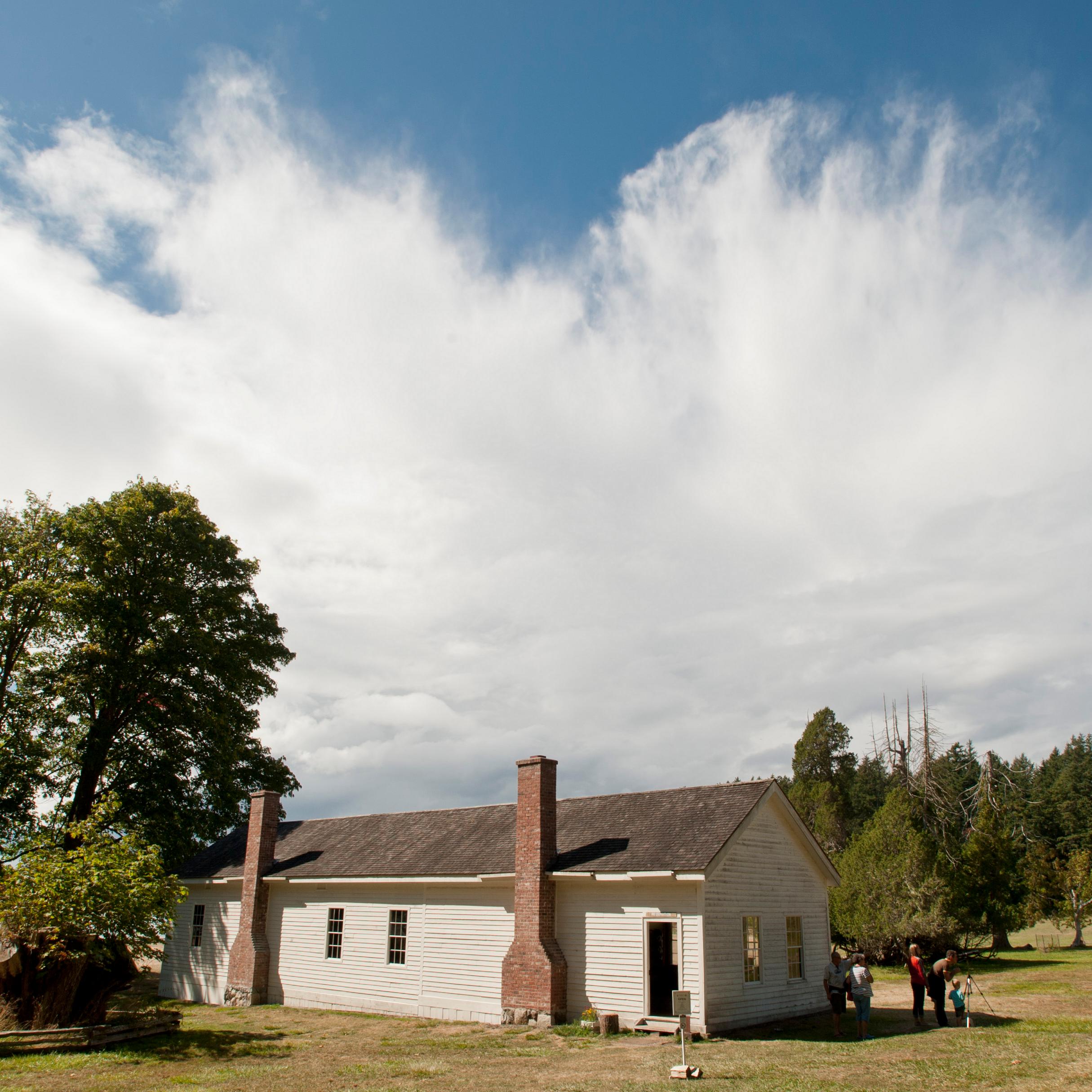 Photograph of a one story 19th century wood frame building with dramatic clouds behind it