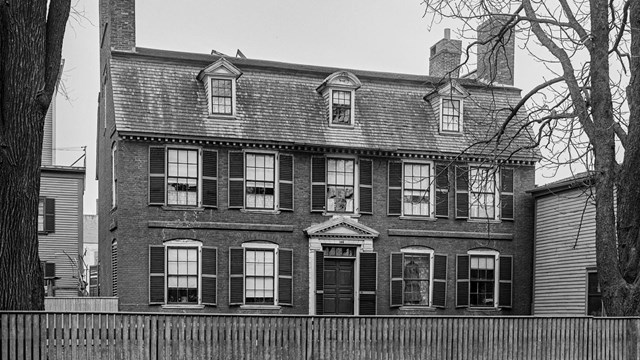 Black and white historic photo of a three-story brick house with two chimneys.