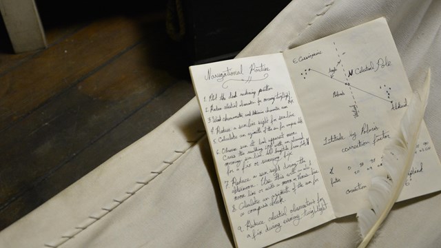 A feather pen rests on an open journal in a sleep hammock.