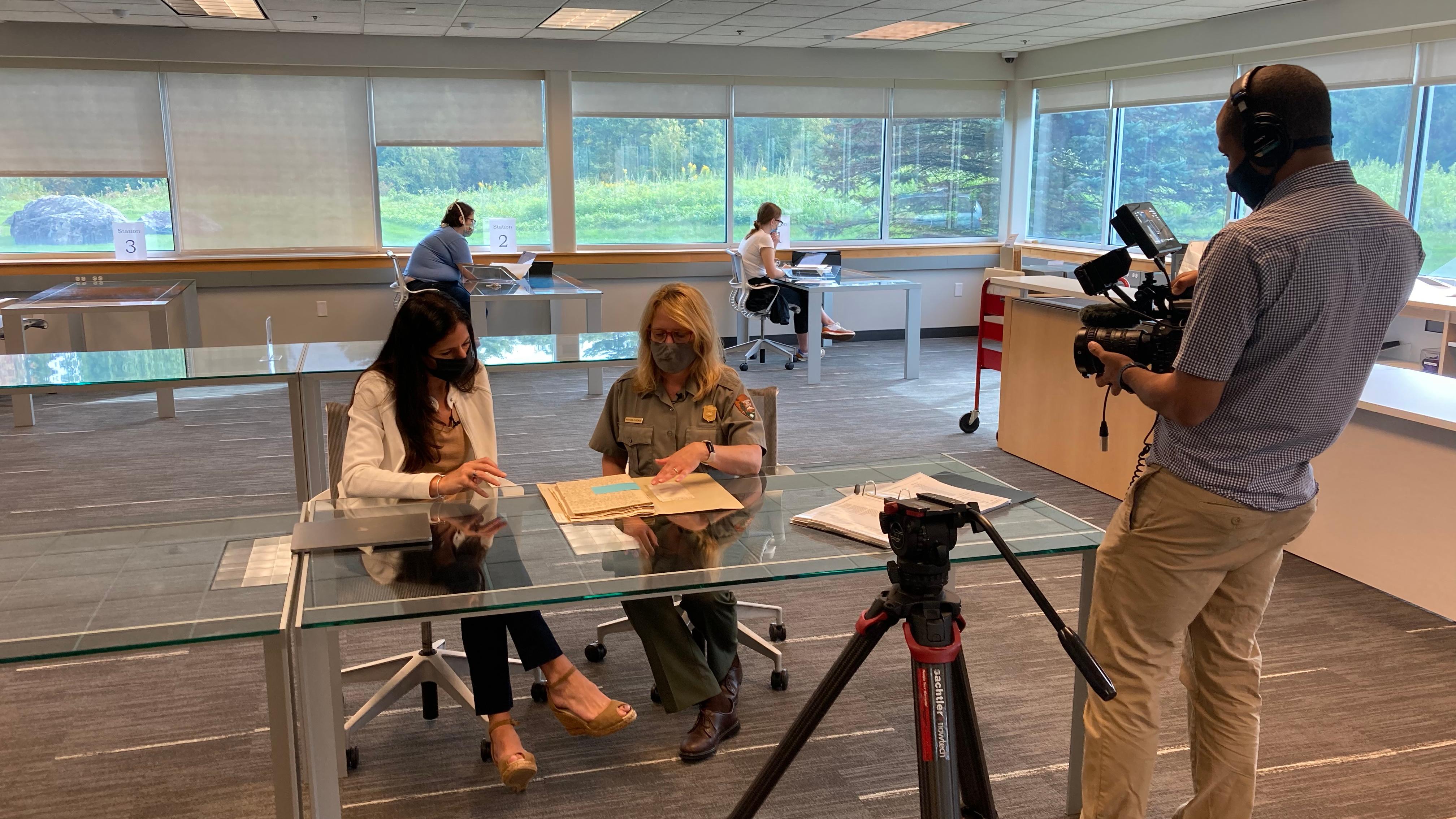 A man films to people sitting at a table. 