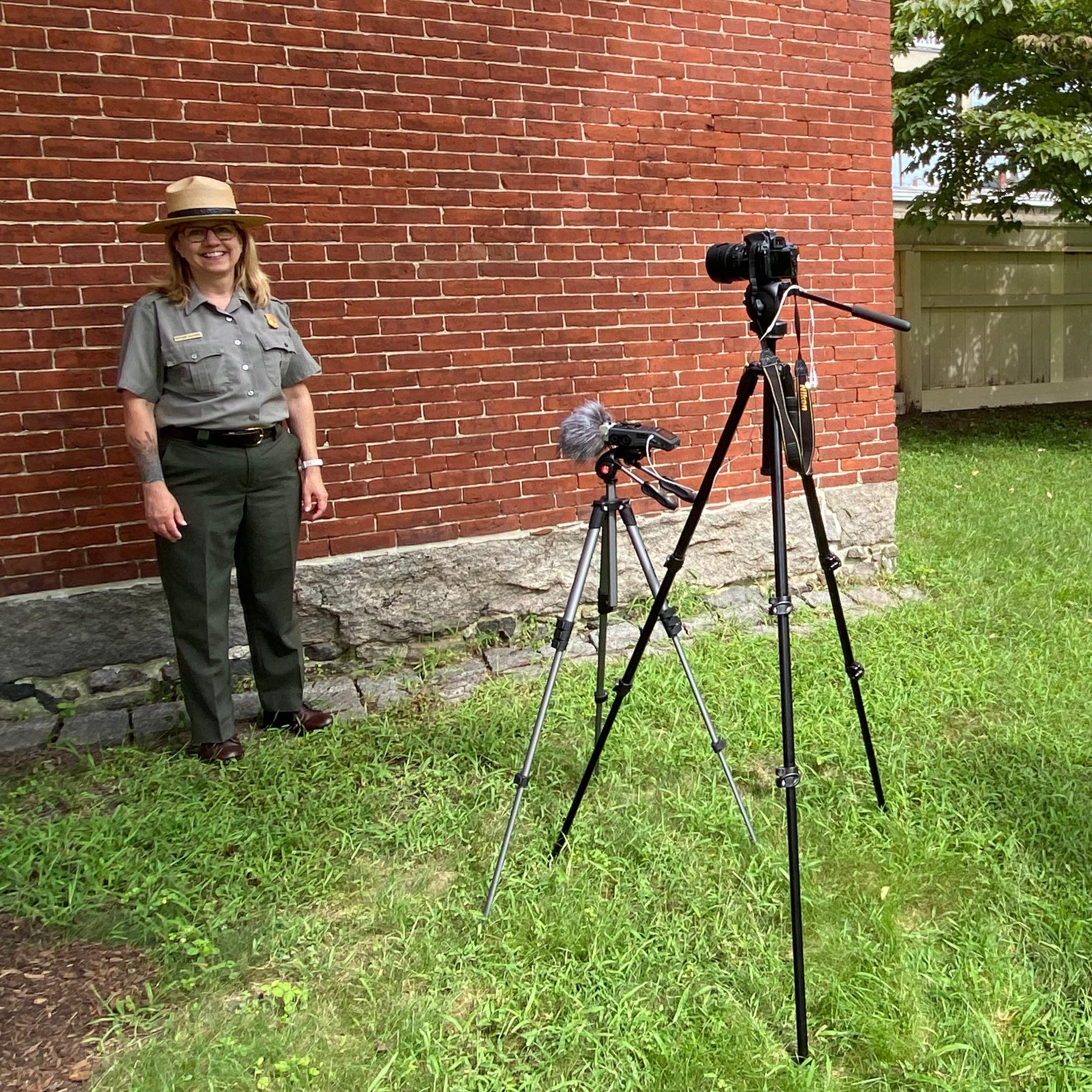 Two rangers prepare to film outdoors by setting up camera, microphone, and note cards.