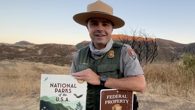 Ranger smiling at the camera holding a children's book.