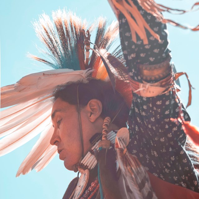 Man dressed traditional regalia arms pointing to the sky mid dance.