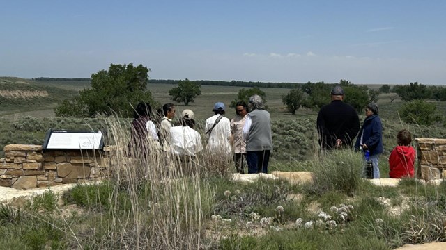 Visitors stand at exhibit panels overlooking a prairie landscape. 
