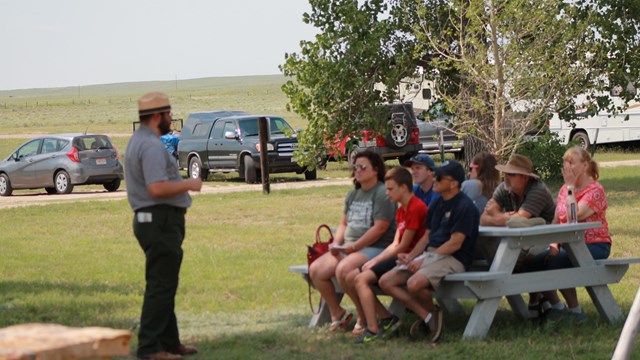 A park ranger speaks to a group seated at a picnic table