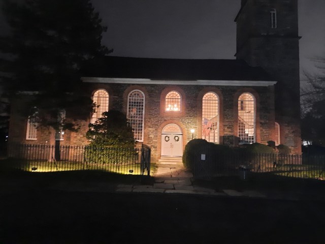 Stone and brick church illuminated with interior and exterior lights.  