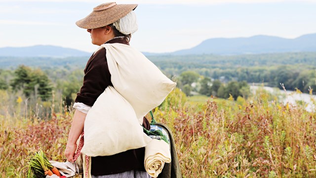 A woman dressed in 18th century clothing stands at an overlook of the Hudson River