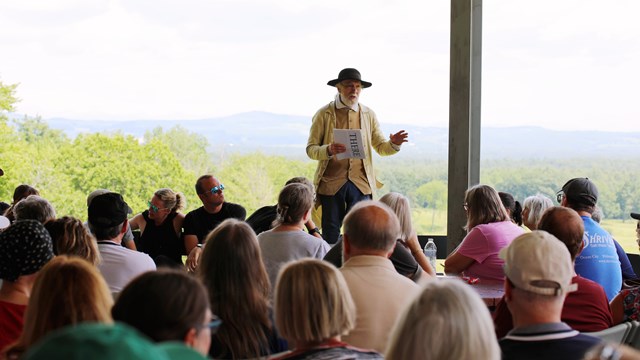 A man wearing 18th century clothing talks to a group of people at the Visitor Center.