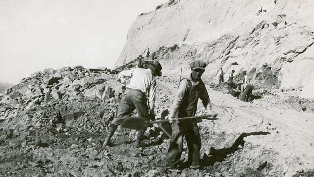 A black and white photo of men building a road with shovels.