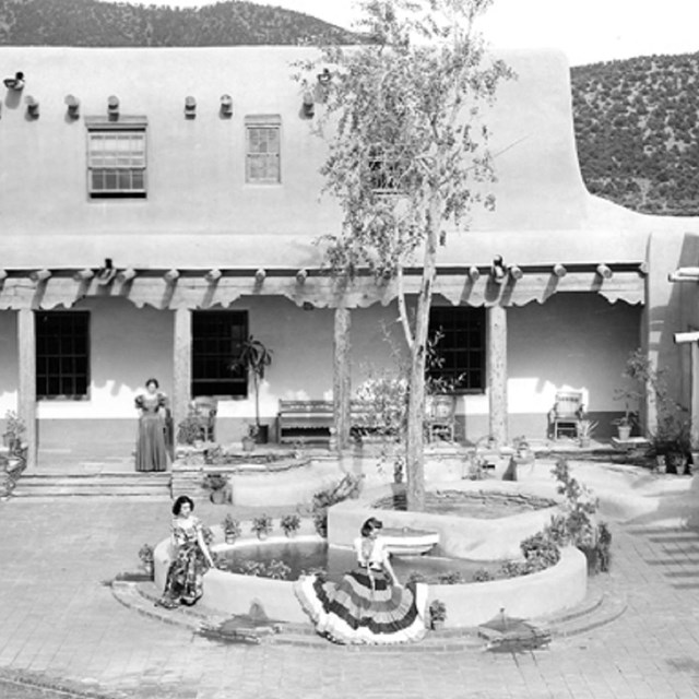 Black and white photo of L shaped Building with colonnade and 3 women sitting in the courtyard.