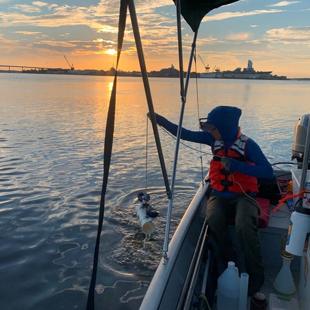 Woman in life vest holds a water sampler over the side of a boat