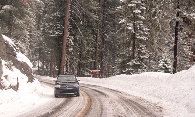 A black car drives down an icy and snowy road.