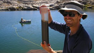 A researcher holds up a core sample near an alpine lake