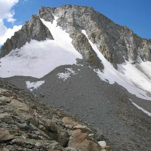 View of a steep rugged mountain with patches of ice and snow that are part of a glacier.
