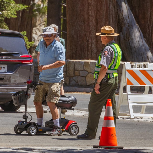 An elderly man standing up from a wheelchair next to a ranger.