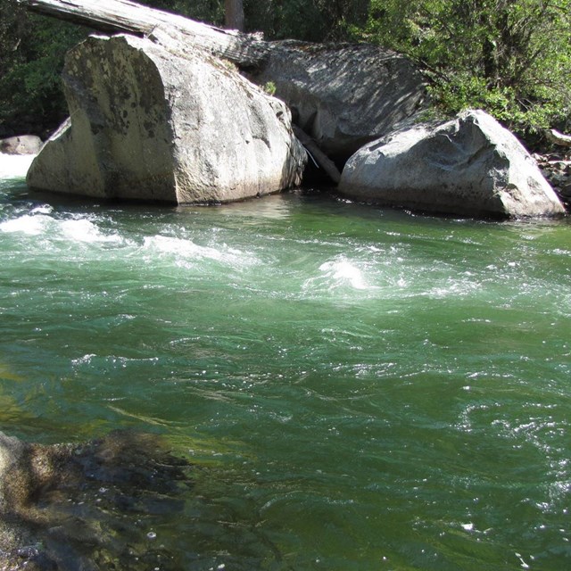Deep blue-green colored river flows past granite boulders.