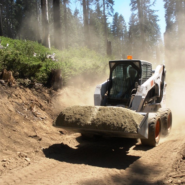 A BobCat earthmover clears the area for trail construction. 
