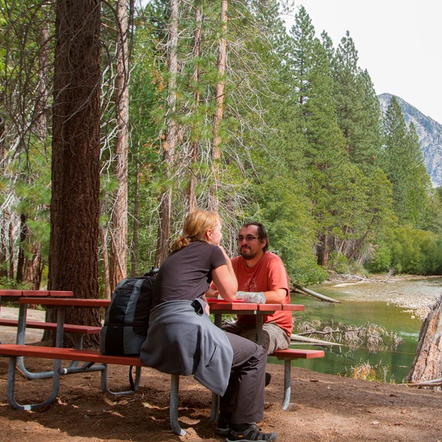 A man and woman sit at a picnic table on the river's edge.