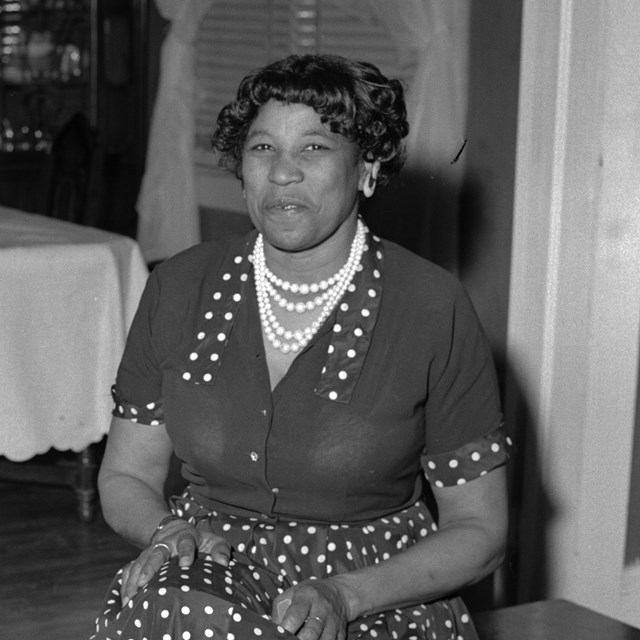Black and white photo of a middle-aged black woman seated and wearing a polka-dot dress.