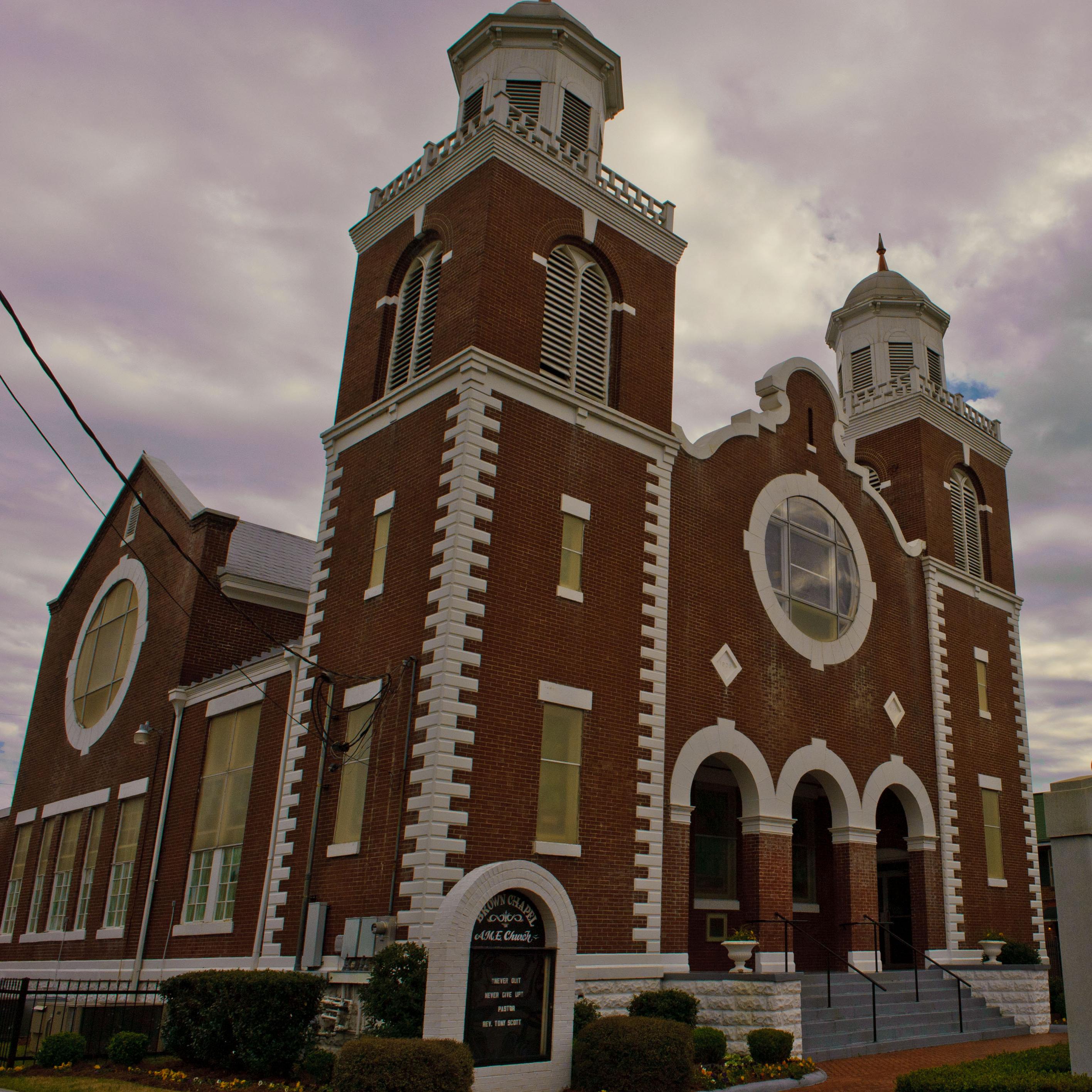 A tall red/brown church building with two towers framing an arched entrance.