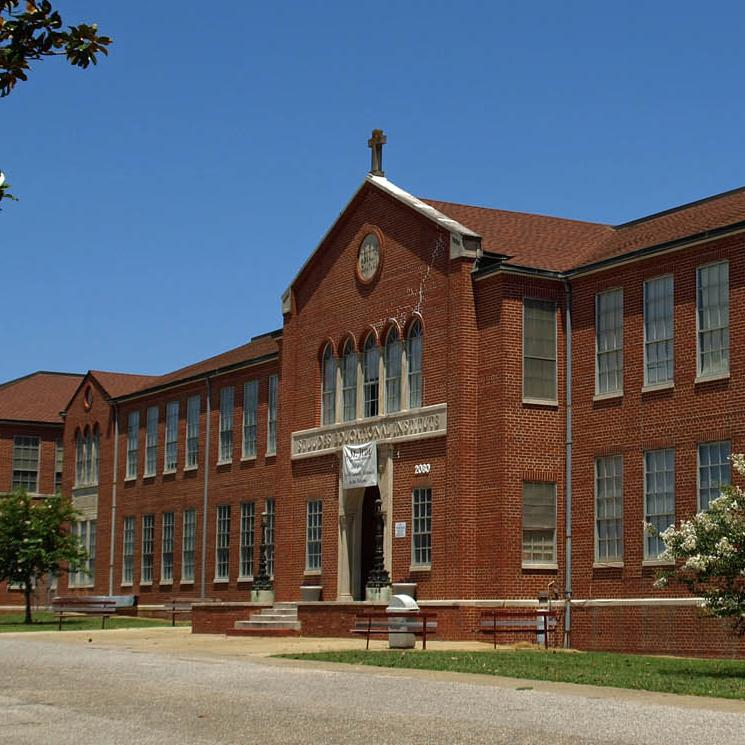 A long two-story brick building with a small stone on the roof above the entrance.