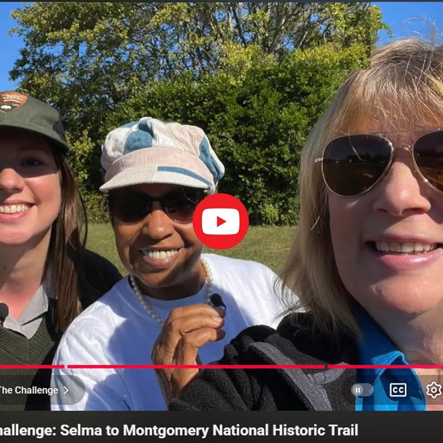 Still of a video showing 3 people smiling, a park ranger, an older black woman, and a white woman.