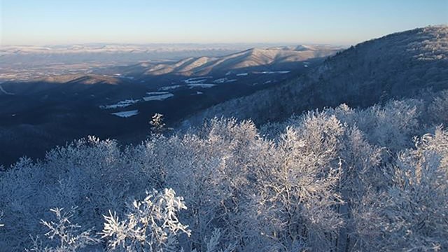 A view from a mountain overlook of trees and mountains covered in ice and snow.