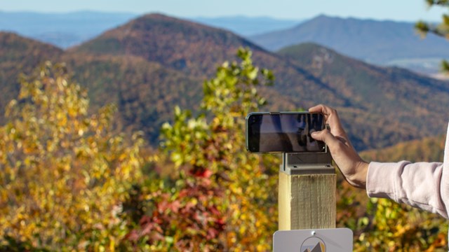 A park ranger takes a picture of a mountain overlook with their cell phone.