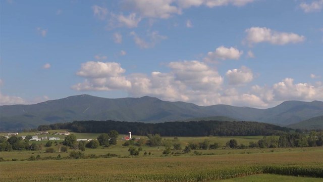 View across green valley, blue ridges and bright blue sky with puffy clouds