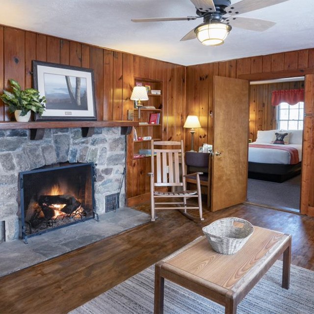 The interior of a lodge with wood walls and a stone fireplace.