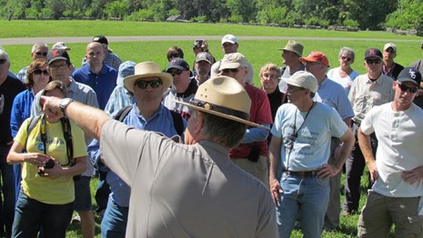A park ranger in flat hat pointing out something to a crowd 