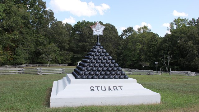 A pyramid of cannonballs sits on a white concrete base the reads Stuat. 