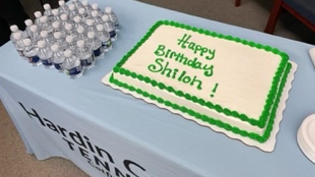 A white and green frosted birthday cake sits on a table. 