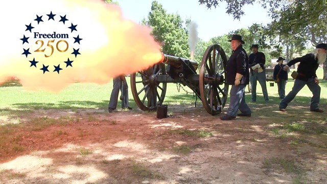 Living historians fire a cannon with Freedom 250 in belching fire. 