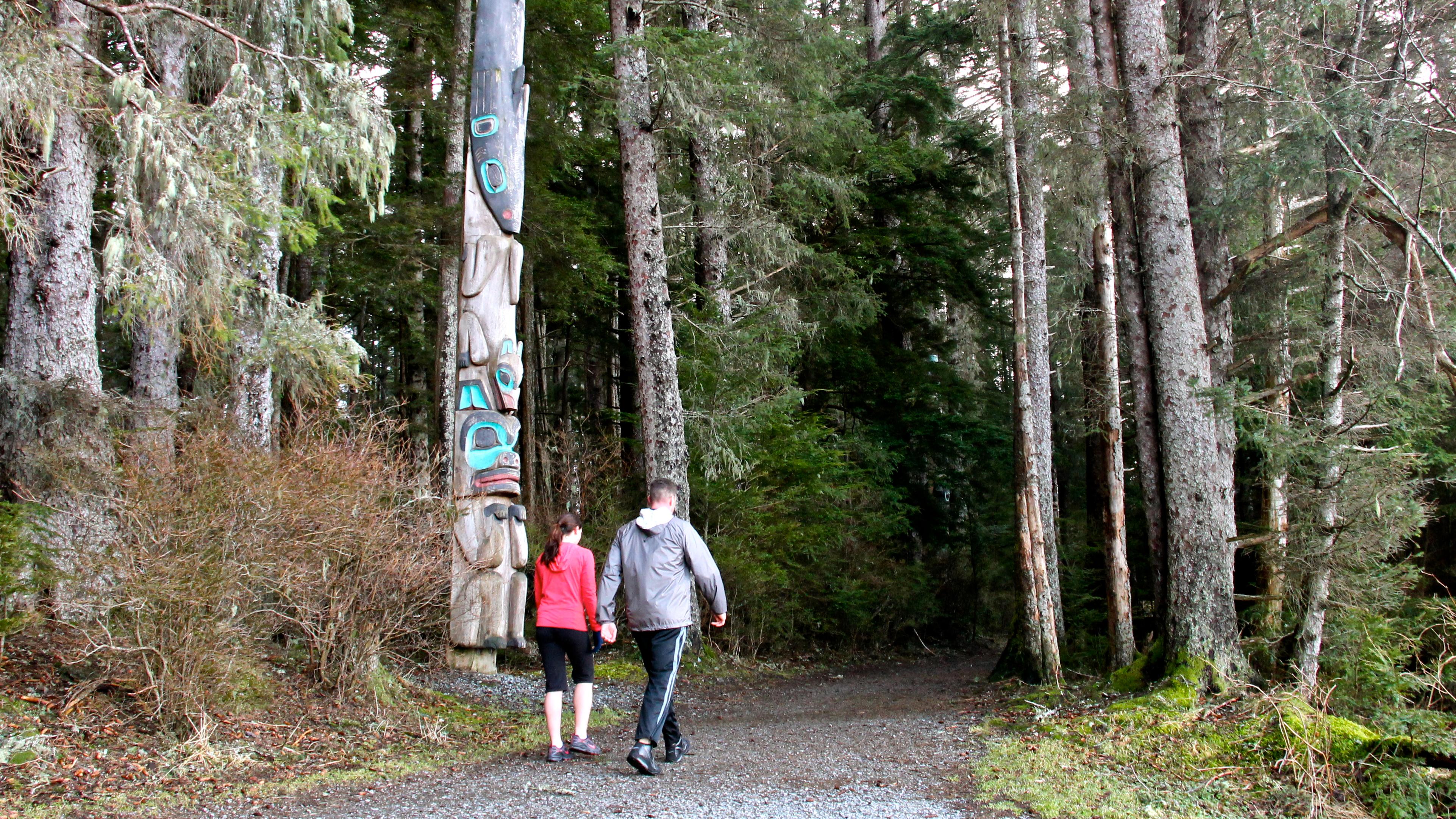 to people walking along a forested trail with a totem pole along the trail