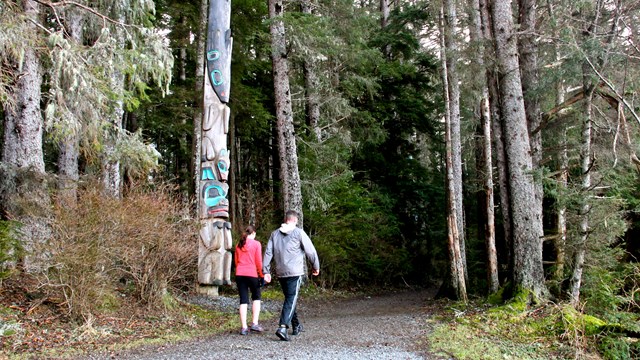 to people walking along a forested trail with a totem pole along the trail