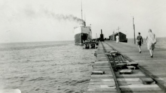 Black and White of a Freighter docked at the end of the Glen Haven Dock, a few people walking toward