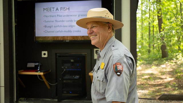 A man in ranger uniform stand in front of a TV screen.