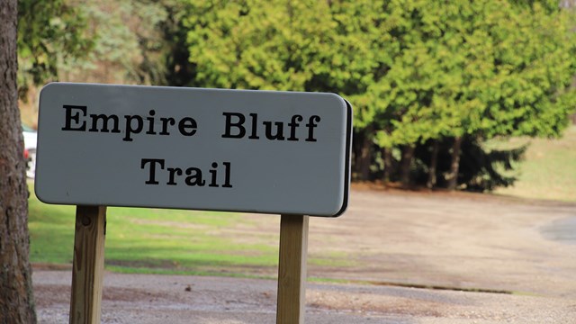 Sign "Empire Bluff Trail" an empty dirt parking lot beckons behind. 