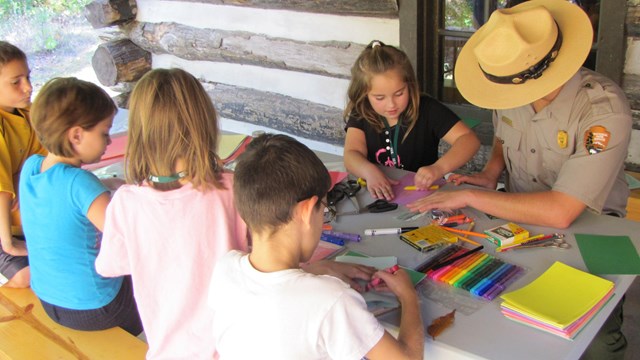 Park Ranger at a table with five children doing crafts.