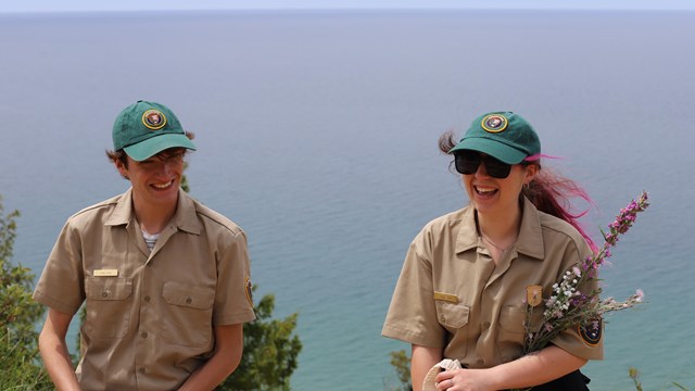 two people wearing volunteer uniforms smile with a large body of water behind them