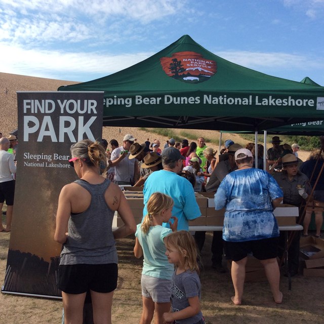 A crowd gathers at the base of a dune where rangers have set up an event tent